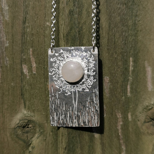 Silver pendant set with a round moonstone. The pendant has a textured, stamped design that represents a flower in a field of grass. this pendant was made by a student on a Stonesetting workshop - one of the jewellery skills workshops that I run.